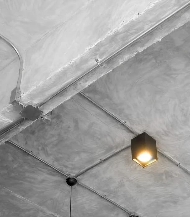 A concrete commercial ceiling with exposed conduit and a boxed light fitting