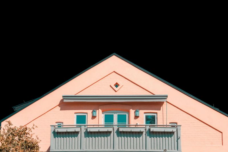A pale pink gable end with teal windows above a slatted balcony